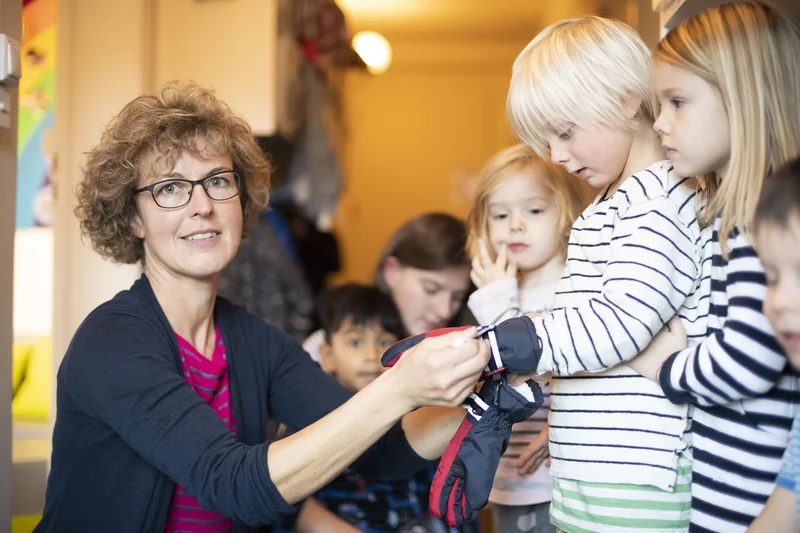 Fachfrau Kinder zieht Kleinkinder Handschuhe an